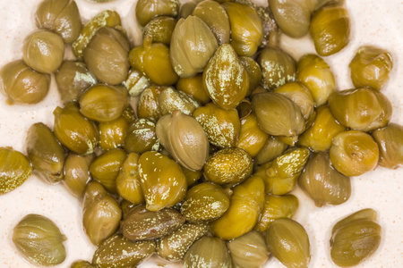 Small heap of pickled capers covered with crystallized white spots of rutin on a saucer, top view close-up in selective focusの写真素材