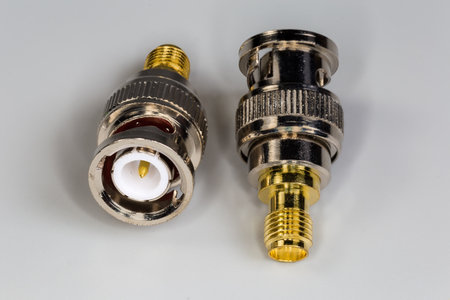 Two high-frequency coaxial adapters with connectors BNC and SMA type on the edges on a gray surface