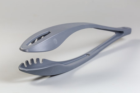 Long handled kitchen locking tongs made with gray food grade plastic on a gray background, view close-up in selective focusの写真素材