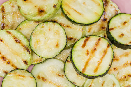 Heap of grilled dark green zucchini and pale green vegetable marrows sliced into circles on dish, top view close-upの写真素材