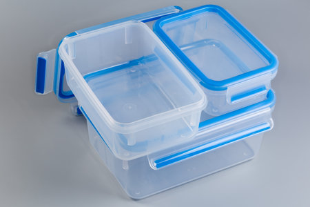 Set of empty reusable transparent plastic food storage containers different sizes closed with blue lids, one of which with removed lid on a gray backgroundの写真素材