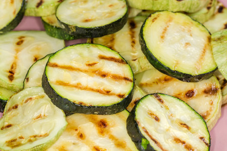 Grilled dark green zucchini and pale green vegetable marrows sliced into circles on dish, view close-up in selective focusの写真素材