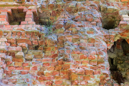 Fragment of the old partly destroyed brick outer wall of a defensive structure in autumn sunny day, bottom view, backgroundの写真素材