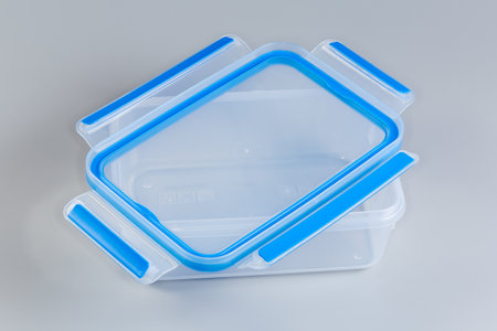 Empty reusable transparent plastic food storage container with unfastened blue lid atop on a gray backgroundの写真素材