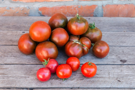 Small heap of whole ripe organic ribbed and ordinary tomatoes kumato and several cherry tomatoes on a foreground on the old rough wooden surfaceの写真素材