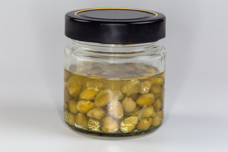 Pickled capers in small jar closed with black lid on a gray background, side view close-upの写真素材
