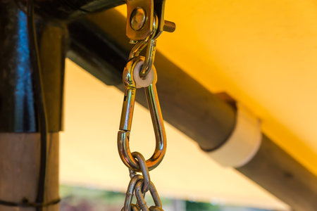 Metal suspension unit consisting of bracket with bolt, hook, suspension carabiner and chain for swing hanging, or swing bench on a blurred background of garden structureの写真素材