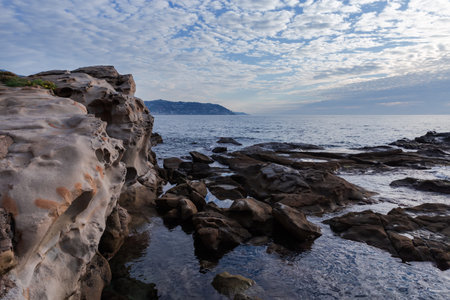 Part of the sea shore with stone coastline on a background of the cloudy sky in overcast morning backlitの写真素材