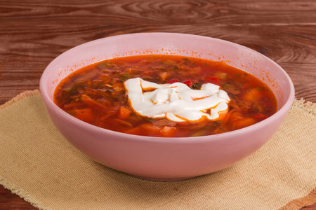 Serving of typical red beetroot Ukrainian borscht seasoned with sour cream in the pink bowl on a rustic table, side view close-upの写真素材