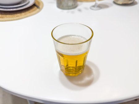 Partially filled small glass of lager beer on a white round table, close-up in selective focusの写真素材