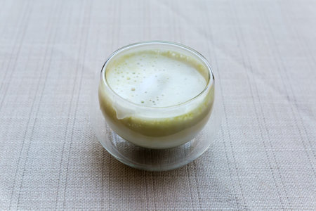 Prepared green tea matcha with coconut milk in small glass cup without handle on table covered with tablecloth close-up in selective focusの写真素材
