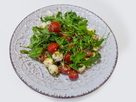 Vegetable salad of mozzarella balls, cherry tomato, arugula and served with pesto sauce and grated parmesan on dish on a white tableの写真素材