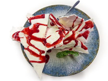 Dessert made with meringue pieces and mascarpone cream cheese, poured over with raspberry jam on the big blue dish, top view on a white backgroundの写真素材