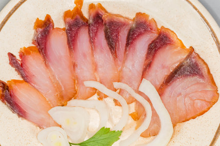 Sliced cold smoked boneless freshwater fish served with fresh onion slices on a saucer, top view...