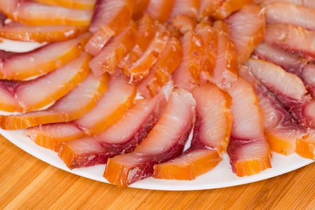Slices of the different cold smoked boneless freshwater fish on a big plate on a wooden surface, fragment close-up in selective focusの写真素材
