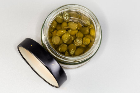 Pickled capers in the small jar with removed black lid beside on a gray background, top view in selective focusの写真素材