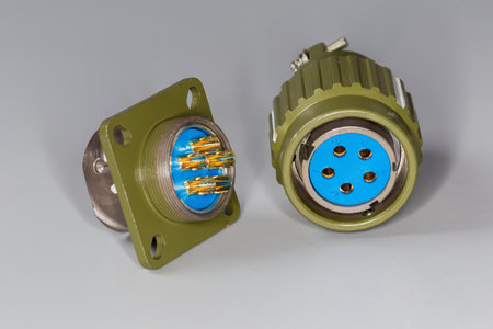Pair of industrial circular metal electrical connectors of plug on square flange with holes for mounting screws with bayonet coupling and straight socket on a gray backgroundの写真素材