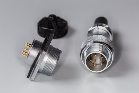 Pair of industrial metal electrical connectors of plug with threaded union nut and socket on square flange with removed protective lid on a gray surface, close-up in selective focusの写真素材