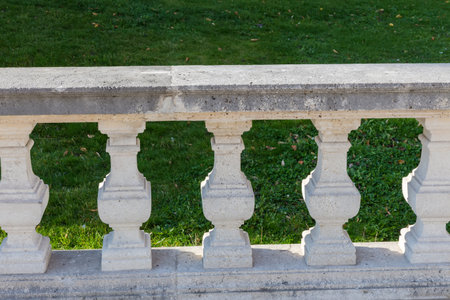 Part of the light stone balustrade with balusters of square section sunlit on a terrace against the grass on lawn in shadeの写真素材