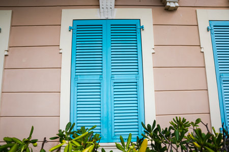 Window with closed wooden shutters painted blue installed in light brown wall, view outdoors in overcast dayの写真素材