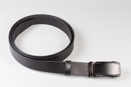 Modern black natural leather belt rolled up with rectangular metal clamping buckle on a gray backgroundの写真素材