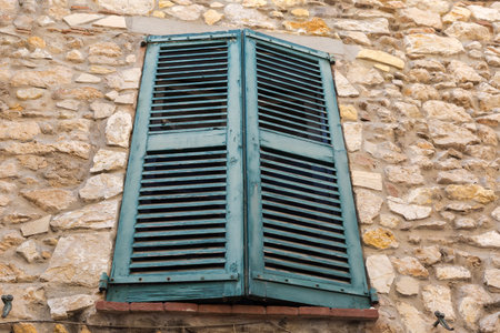 Old green wooden exterior shutters with fixed louvers covered up installed on a window in the rough stone building wall, bottom view in overcastの写真素材