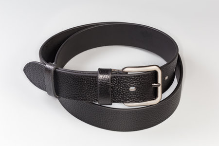 Fastened black leather belt partly rolled up with conventional classical metal buckle with...