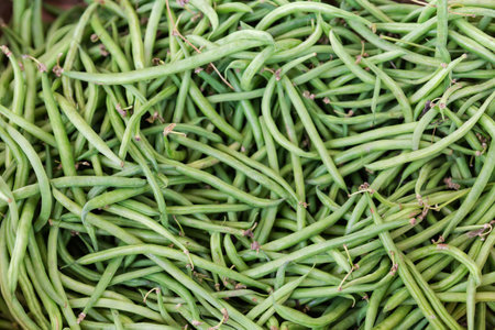 Freshly harvested green beans in a container for sale in a vegetable market, top view in selective...