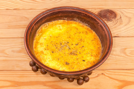 Hot scrambled eggs in clay bowl freshly prepared stands on a hot stand on a rustic wooden tableの写真素材