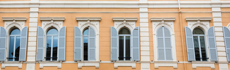 Row of arched windows with open and closed wooden shutters painted white in yellow wall, panoramic...