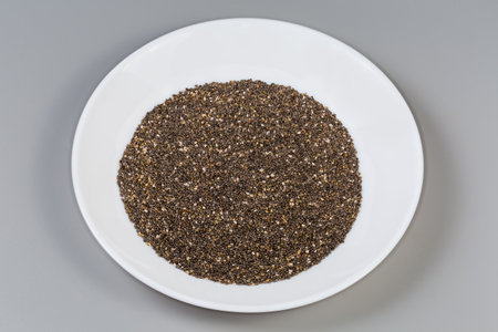 Heap of the raw gray-brown spotted chia seeds on a white dish on a gray backgroundの写真素材