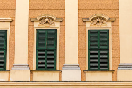 Row of windows with closed wooden shutters painted dark green in yellow wall outdoors in overcast dayの写真素材
