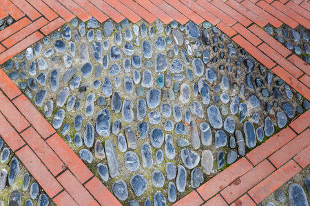 Part of footpath paved with dark small cobblestones and red bricks, top view in overcast day