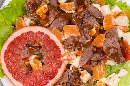 Salad made with slices of boiled duck meat, diced mozzarella, different fresh citrus, vegetables and greens, top view close-upの写真素材