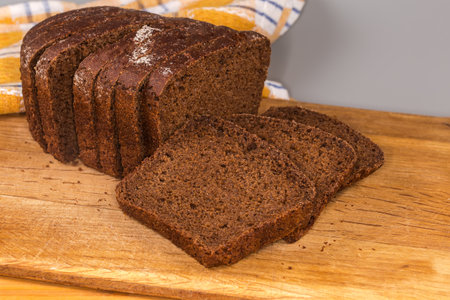 Sliced rectangular oblong loaf of the brown bread from rye and wheat flour on the wooden cutting board, front view close-up in selective focusの写真素材