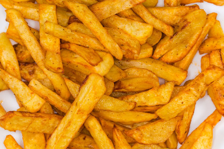 Heap of the French fries in form of elongated pieces on dish, top view close-up in selective focus