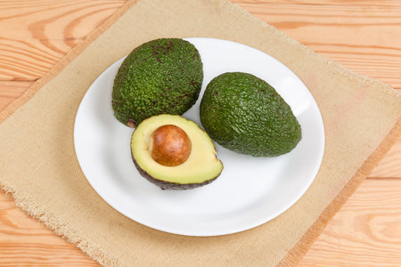 Two whole and one half of avocado with seed and dark green skin  on a dish on a rustic table