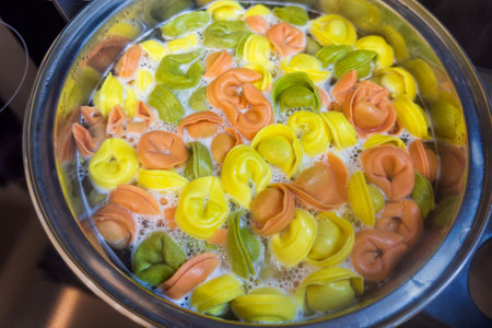 Dumplings with meat stuffing and multicolored dough during boiling in the stainless steel pot on a stove top, top viewの写真素材
