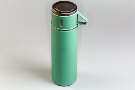 Small light green metal domestic vacuum flask closed with lid in form of cup with handle on a gray backgroundの写真素材
