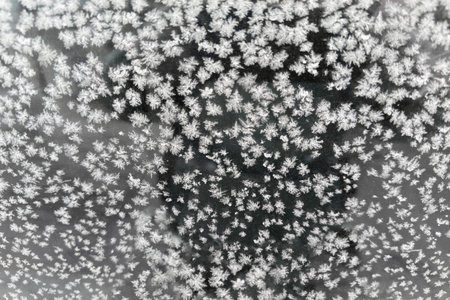 Texture of the hoarfrost on the surface of side window of parked car at overcast morning, view...