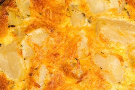 Surface of the appetizing browned crust of the melted cheese on the top of freshly prepared potato casserole in bowl, top view close-upの写真素材
