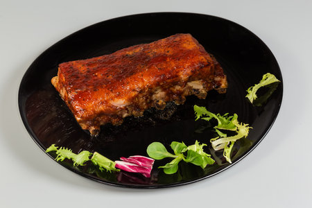 Whole piece of the pork ribs baked with spices and special sauce on the big black plate on a gray backgroundの写真素材