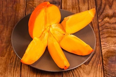 Ripe dissected persimmon on the brown dish on a wooden rustic tableの写真素材