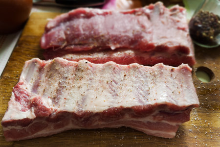 Two big whole pieces of the raw pork ribs sprinkled with salt and spices on an old wooden cutting board, front view close-up in selective focusの写真素材