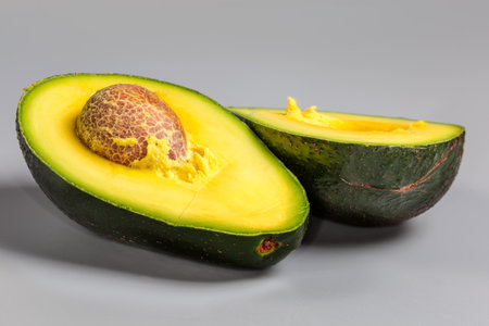 Two halves of ripe avocado one of which with seed, with dark green skin on a gray background, front view close-up in selective focusの写真素材