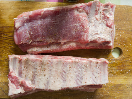 Two big whole pieces of the raw pork ribs sprinkled with salt and spices on an old wooden cutting board, top viewの写真素材