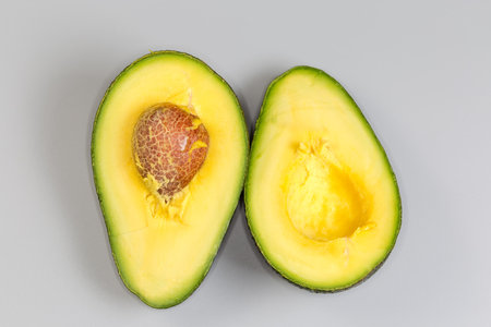 Two halves of ripe avocado one of which with seed, with dark green skin on a gray background, top view close-upの写真素材