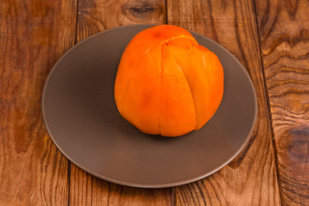 Ripe dissected persimmon on the brown dish on a wooden rustic tableの写真素材