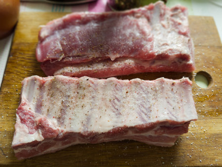 Two big whole pieces of the raw pork ribs sprinkled with salt and spices on a wooden cutting board, close-up in selective focusの写真素材