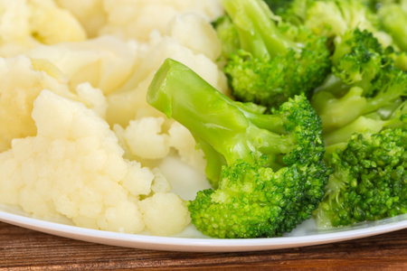 Freshly boiled small pieces of broccoli and cauliflower on the white dish, front view close-up in selective focusの写真素材